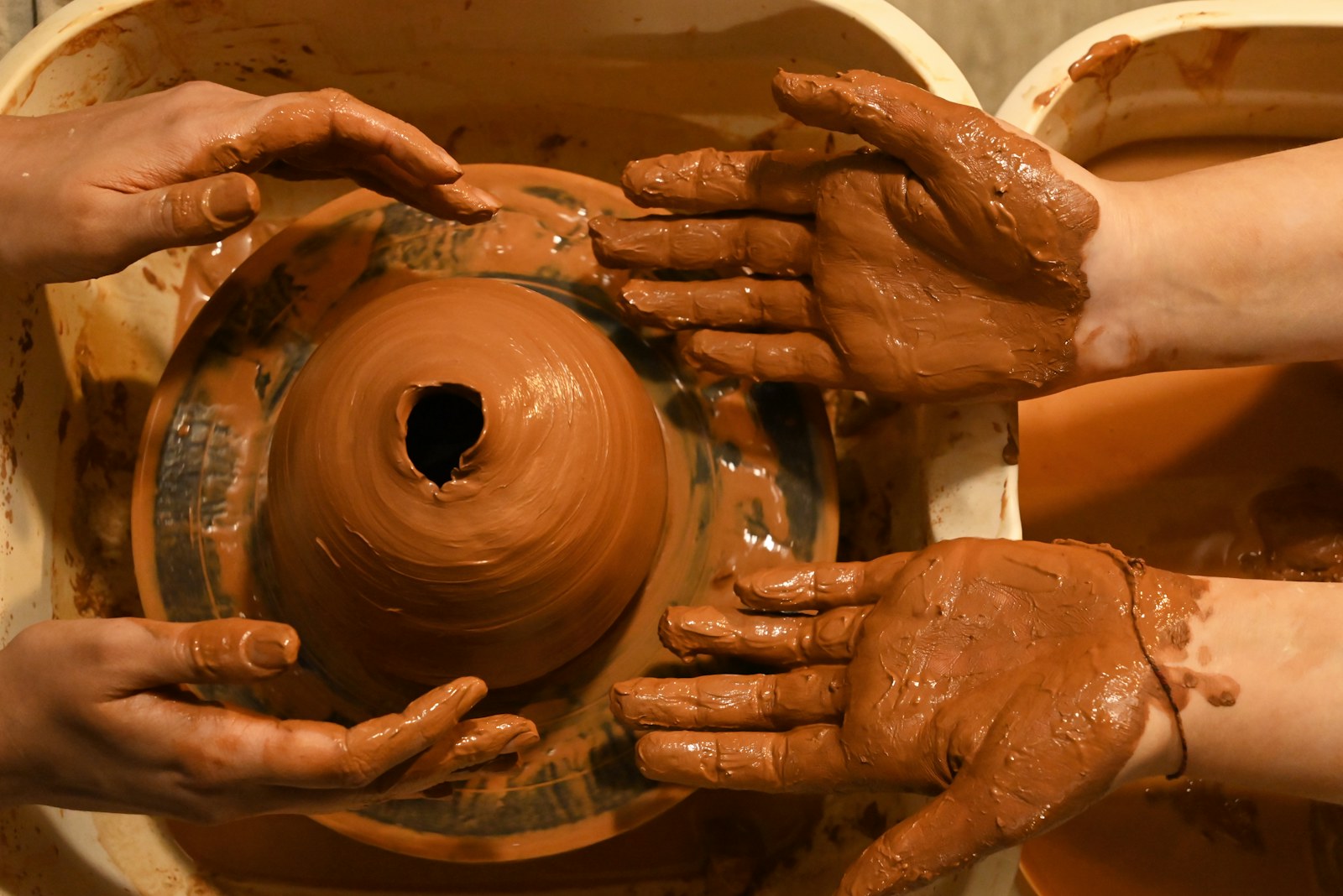 Hands shaping clay together on a pottery wheel